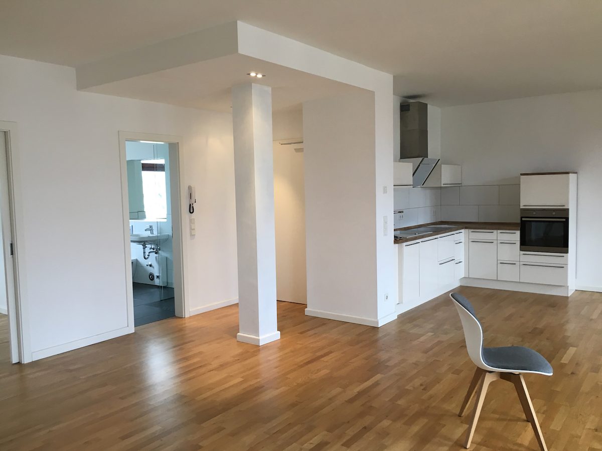 Espacio vacío con cocina abierta blanca y piso de madera